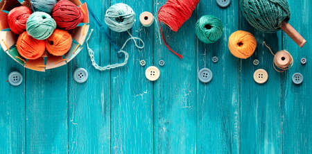 Decorative border made of wool bundles, yarn balls, buttons and cord. Latch and knitting needles. Creative flat lay, top view on distressed turquoise blue wood boards, copy-space, place for your text.の写真素材