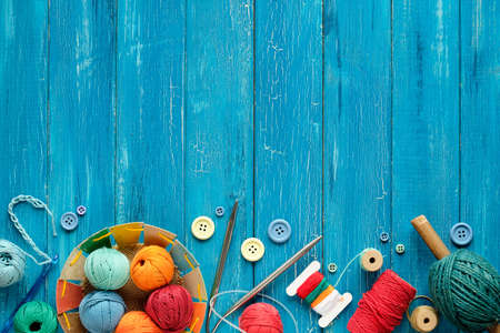 Decorative border made of wool bundles, yarn balls, buttons and cord. Latch and knitting needles. Creative flat lay on aged turquoise blue wood boards, copy-space, place for text.の写真素材