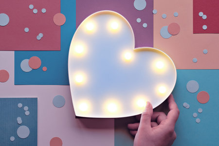 Hand holds heart shaped lightbox. Abstract geometric layered paper background with trendy circles,...