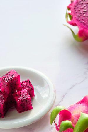 Pink dragon fruit, pitaya or pitahaya cut in cubes on white plate. Trendy superfood ingredient. Close-up on the slices, fruit cubes in white plate, copy-space.の写真素材