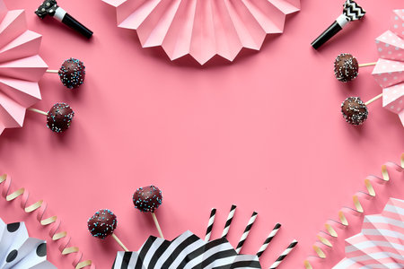 Decorative frame with copy-space. Chocolate cake pops covered with colored sugar icing. Creative monochrome flat lay on pink paper with folded paper fans, confetti, sugar hearts, stripy drink straws.の写真素材
