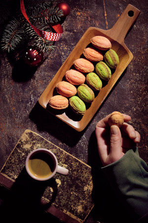 Walnut shaped cookies with Dulce De Leche or sweetened condensed milk. Creative flat lay on dark table decorated with fir twigs, cones, red ribbons, cup of coffee on old book. Hand with cookie.の写真素材