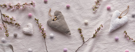 Hand made textile hearts and balls on cotton background. Monochromatic look, panoramic banner composition. Textile handicraft in neutral colors. Winter cherry flower twigs.の写真素材