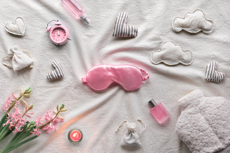 Healthy night sleep creative concept. Off white, ivory textile background. Pink hyacinth flowers, alarm, pink essential oil. Orthopedic pillow, sleep mask, tea, candle and warm bottle.の写真素材