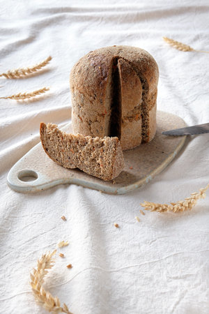 Dinkelbrot in German that means spelt. Loaf of wholemeal dinkel rye bread. Dinkel or Spelt is an ancient grain, alternative to wheat. Off white, ivory textile tablecloth.の写真素材
