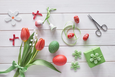 Flat lay with red tulips in rattan wreath basket and green grass. Decorative painted Easter eggs....