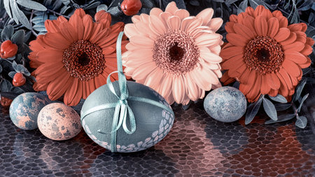 Single colored Easter egg with green ribbon bow on dark background with Springtime flowers, herbera...