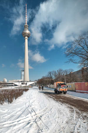 BERLIN, GERMANY FEBRUARY 10, 2021: Berlin under snow. Panoramic image of Alexanderplatz with famous TV tower covered with snow. Orange snow cleaning car.のeditorial素材