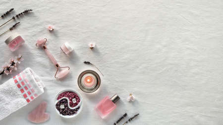 Crystal rose quartz facial roller, Gua sha stone for face massage. Flat lay on off white textile. Handmade aromatic salt.,dry lavender. Essential oil, sn care products. Panoramic image, copy-space.の写真素材