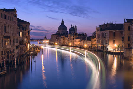 Romantic Venice at night. Cityscape image of Grand Canal in Venice, with Santa Maria della Salute Basilica reflected in calm sea. Lights of passenger boat on the water.の写真素材