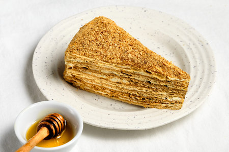 Russian honey cake slice on white plate on off white textile tablecloth. Traditional 8 layer...