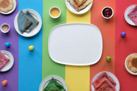 Rainbow pancakes, different color crepes. Spinach, beetroot powder, blue matcha and turmeric crepes. Colorful pancakes, flat lay on rainbow layered paper background. Copy-space, place for text.の写真素材