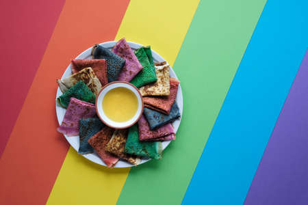 Rainbow pancakes, different color crepes. Spinach, beetroot powder, blue matcha and turmeric crepes. Colorful pancakes, flat lay on rainbow layered paper.の写真素材