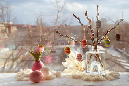 Easter decorations on windowsill in Spring. Wooden painted eggs on pussy willow twigs, Easter eggs, hyacinth with bulbs in wax, macrame mats. Window with urban view on sunset. Happy Easterの写真素材