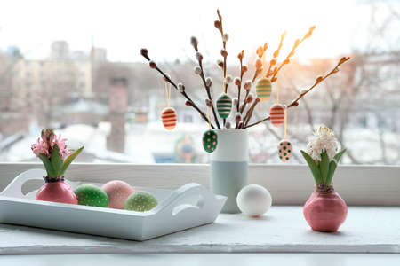 Easter decorations on windowsill, panoramic image. Wooden painted eggs on pussy willow, hyacinth flowers, bulbs in pink wax. Window, urban view. Easter eggs in white tray. Happy Easter.の写真素材