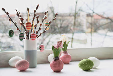 Easter decorations on windowsill, panoramic image. Wooden painted eggs on pussy willow. Hyacinth flowers with bulbs in pink wax. Window, view over town. Romantic indoor setup. Happy Easterの写真素材