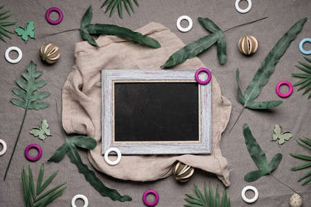 Jungle floral flat lay on earth-colored natural linen textile. Blackboard, chalk board, text space. Tropical plants, exotic fern, palm leaves. Lush greenery, quail feathers, dry lime fruit, wood ringsの写真素材