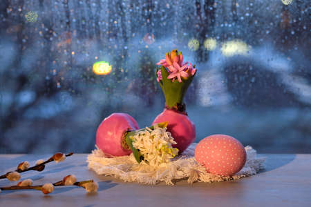 Evening window in Spring, hyacinth with onion in wax and painted Easter eggs and pussy willow twigs. Window with blue evening light and rain drops. Romantic indoor setup.の写真素材