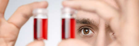 Young male medic or researcher holds up liquid samples. Shallow DOF, focus on the face. This image is toned.の写真素材