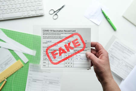 Fake covid vaccination record card. Covid scams.Forged health certificate with false vaccination record against covid-19. Blank card, pen, paper knife,laminator. Top view, flat lay .の写真素材