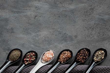Various spices in ceramic oriental spoons and pinch bowls on dark grey. Textile towel on textured background. Flat lay, top view with copy-space. Various dry herbs, pepper, salt, crispy chili, thyme.の写真素材