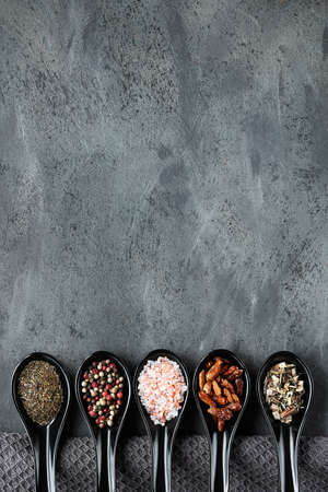 Various spices in ceramic oriental spoons and pinch bowls on dark grey. Textile towel on textured background. Flat lay, top view with copy-space. Various dry herbs, pepper, salt, crispy chili, thyme.の写真素材