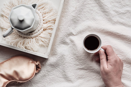 Espresso in hand, tray with white ceramic espresso coffee maker on trendy macrame pad.