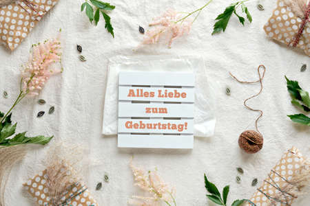 Text Alles Liebe zum Geburtstag means happy Birthday in German language. Gifts wrapped in beige craft paper. Dry wild grass and pink Astilbe flowers. Flat lay on off white textile .の写真素材