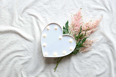 Heart lightbox and wild flowers . Flat lay on off white textile. Natural materials, environment concious, low impact lifestyle. Pale pink Prachtspiere flower.の写真素材