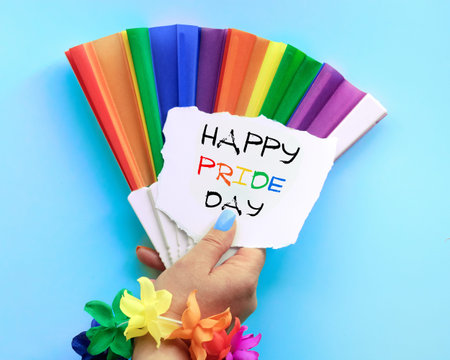 Text Happy Pride Day on torn paper in hand with fake nails. Rainbow fan in colors of the rainbow,...