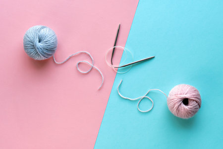 Wool yarn balls and knitting needles with string on split pink and mint blue paper background. Creative minimal simple flat lay, top view, craft concept arrangement.の写真素材