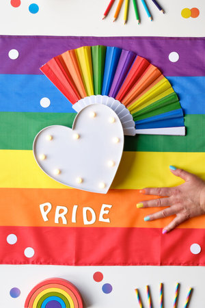 Rainbow LGBT flag background with frames, fan, pencils and ribbons. Hand with painted nails....