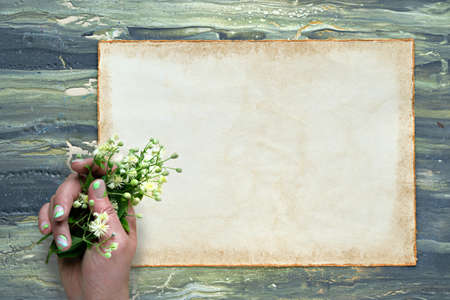 Text Alles Gute zum Geburtstag means Happy Birhday in German. Greeting on aged patchment, beige paper page. Hand with pale yellow flowers. Flat lay on aged textured painted green brown background.の写真素材