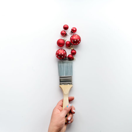 Painting brush in hand, red paint from Christmas baubles, balls, Xmas trinkets. Creative simple...