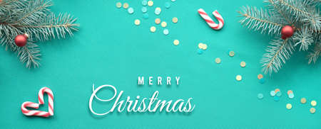Christmas banner panoramic background. Text Merry Christmas on turquoise textile. Top view on fir twigs with Xmas red decorations, hearts, candy canes.の写真素材