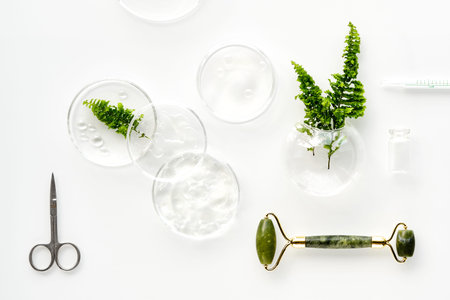 Self made moisturizer and green jade face roller. Exotic fern leaves and water drops on white...