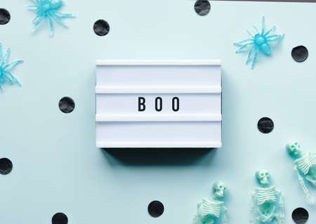 Halloween decor and word Boo written on text box. Minimal Halloween background with pale green skeletons and black paper confetti, polka dots. Flat lay, top view on mint green background.の写真素材
