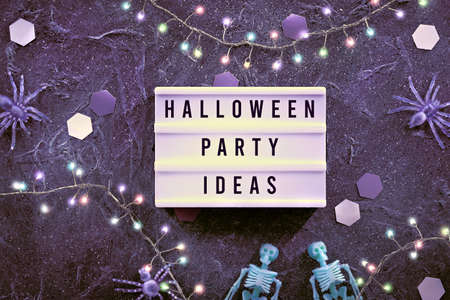 Halloween decor and Halloween Party Ideas written on text box. Minimal Halloween background with pale green skeletons and purple spiders. Dark background with paper hexagons and lights on garland.の写真素材