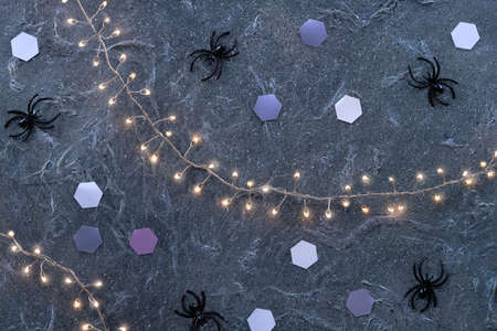 Minimal Halloween background with pale mint green spiders glow dark purple textured background . Flat lay, top view on background with paper hexagons and garland with lights.の写真素材