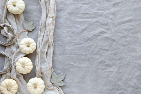 Autumn background with natural pumpkins and decorative grey concrete maple leaves. Flat lay, top view on grey uncolored linen textile. Fall background with decorative border, copy-space.の写真素材