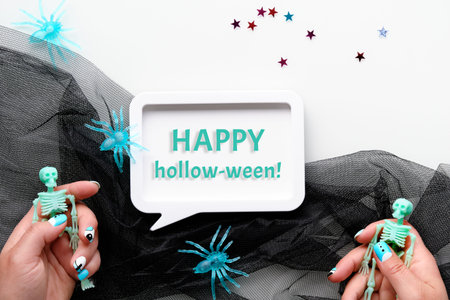 Halloween flat lay with hands and spiders. Text Happy hollow-ween in white frame. Skeletons in hands...