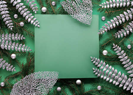 Green silver Christmas background with square copy-space, place for text. Natural Xmas twigs decorated with silver exotic deco leaves and glass baubles, balls. Flat lay on dark green paper.の写真素材