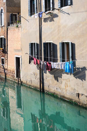 Washing lines along canal in Venice, Italy with reflection in water. Laundry hanging on a clothes line between city buildings. Laundry hanging between windows of old brick houses in Venice.の写真素材
