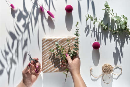 Eco friendly decorations - recycled craft wrapping paper, dry pampas grass, fresh natural eucalyptus twigs and dried bunny tails. Wrapped gift box with natural Christmas decor in female hands.の写真素材