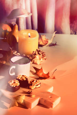 Chocolate pralines with walnut nuts on marble cutting board. Closeup on candy. Autumn arrangement with candle, pumpkins, wooden mushroom and ginkgo leaves. Natural sunlight, long shadowsの写真素材