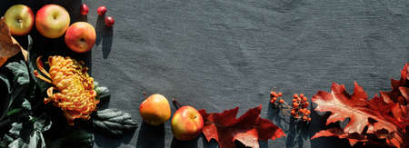 Orange chrysanthemum flowers, dry bunny tail grass and red oak leaves. Autumn decorations, top view with copy-space. Flat lay on dark textile.の写真素材