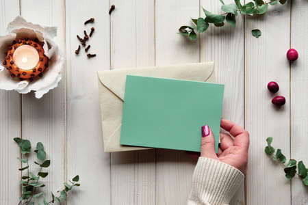 Blank postcard in hand. Winter holiday greeting card mockup. Eucalyptus, tea light in pomander ballの写真素材