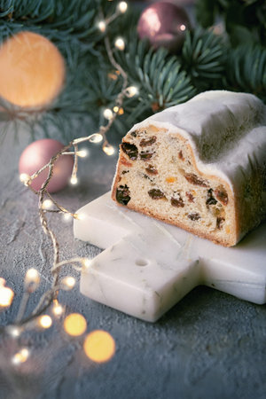 Christmas stollen on grey stone background with garland, Xmas lights, on fir twigs.