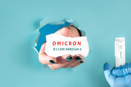 Omicron, new corona virus variant of concern. Paper hole with human hand showing scrap of paper with...