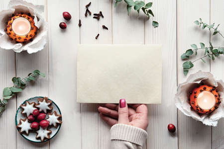 Blank postcard in hand. Winter holiday greeting card mockup. Eucalyptus, tea light in pomander ballの写真素材